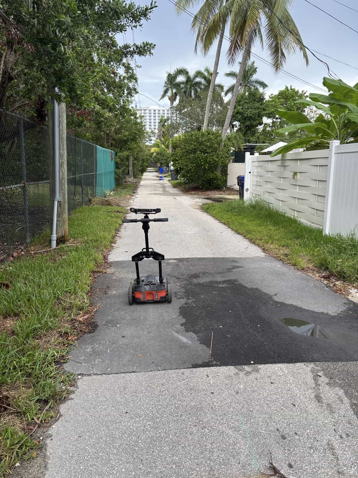 Scooter on sidewalk with patchwork repair and lush greenery.