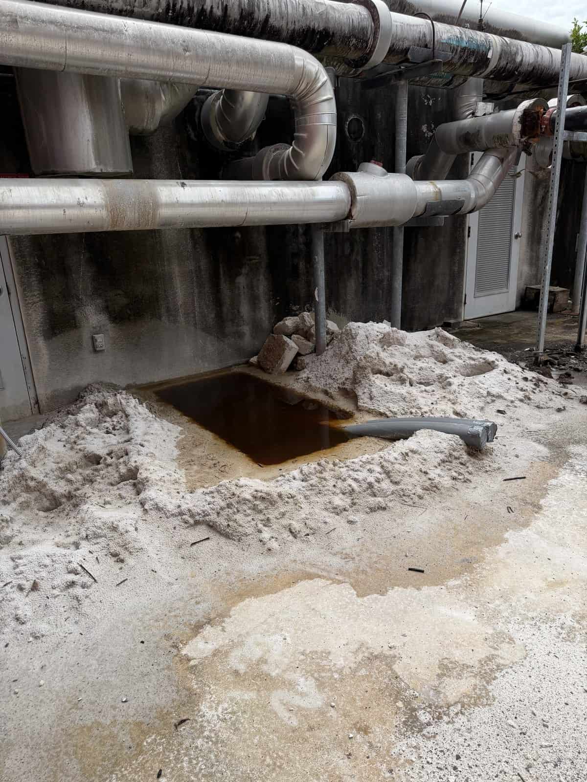 Industrial pipes with a spill of dark liquid on concrete floor.
