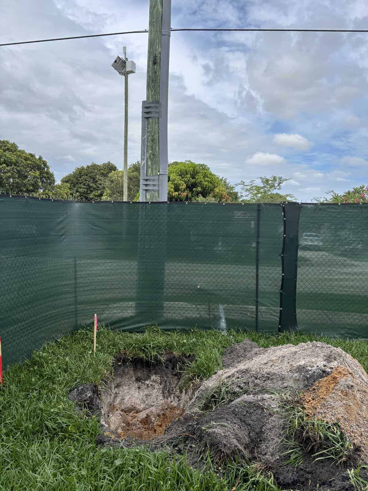 Construction site with green safety fence, rocks, and cloudy sky.