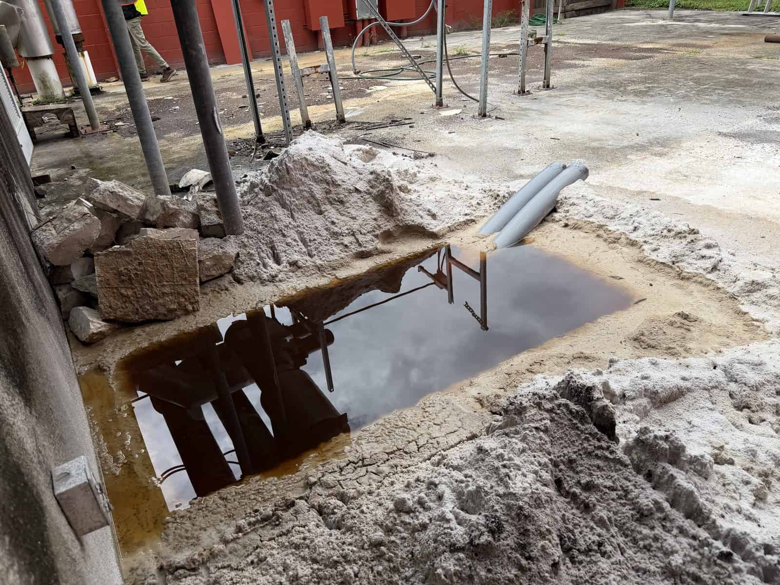 Construction site with water pool and pipes, safety barriers, and building materials.