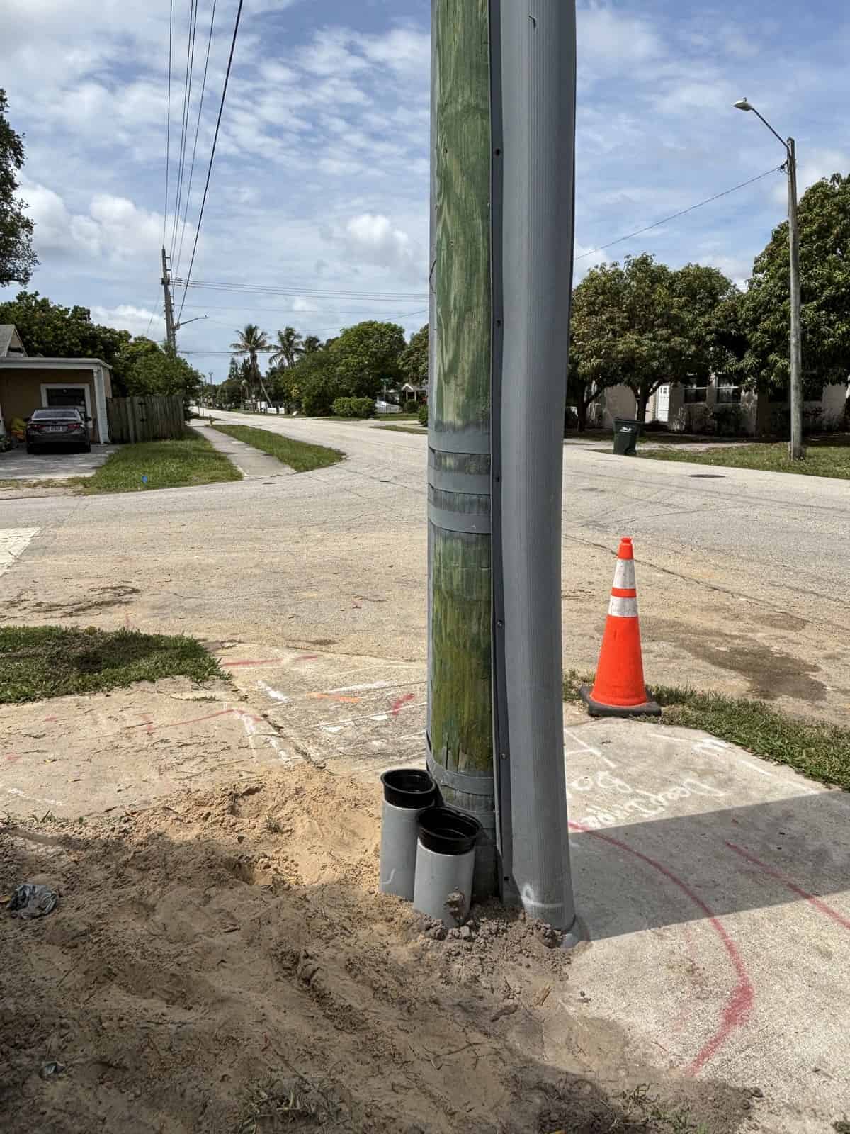 Utility pole with pipes at base on a residential street under blue sky.
