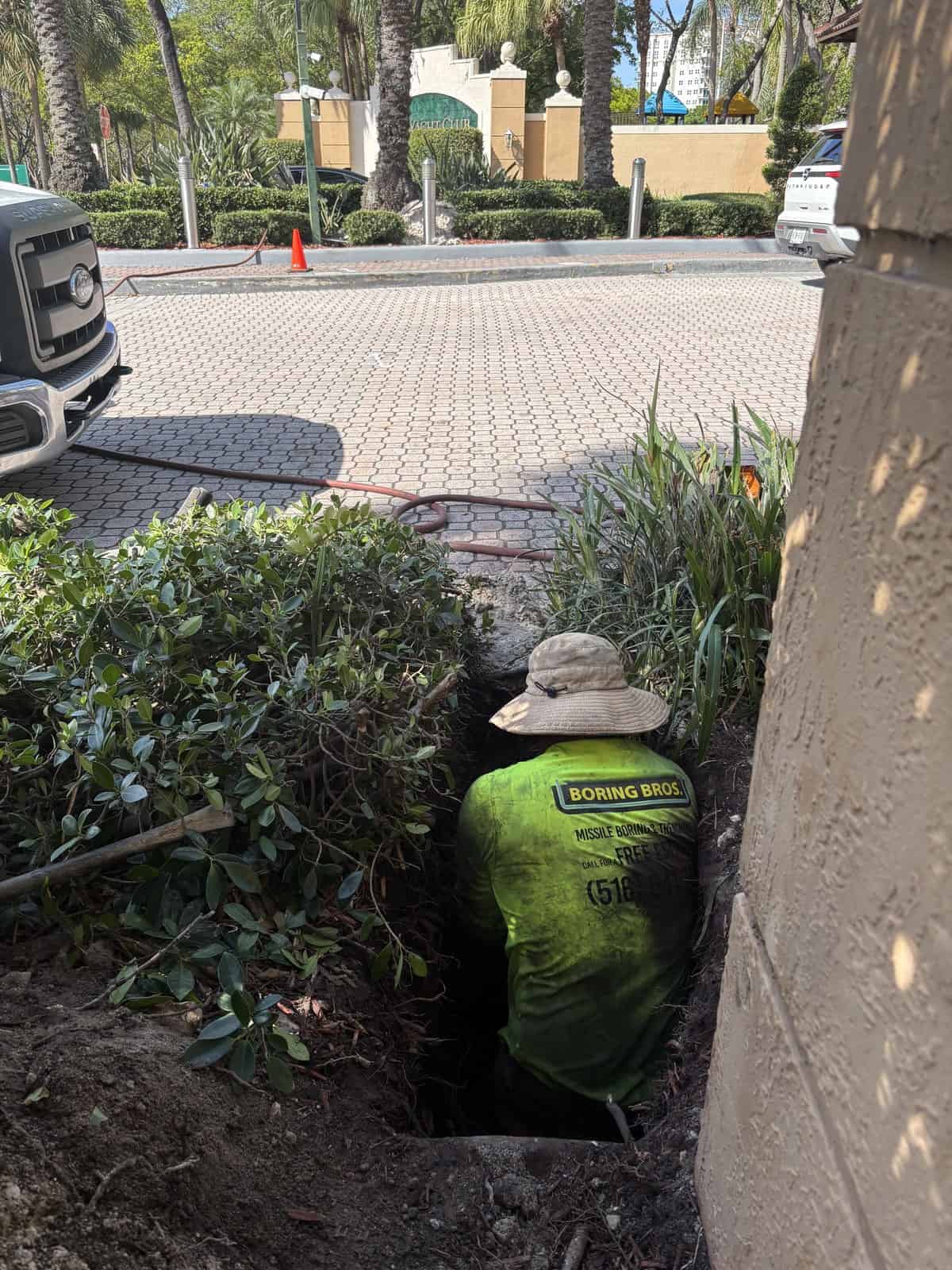 Worker from Boring Bros installing underground utility line in a garden.