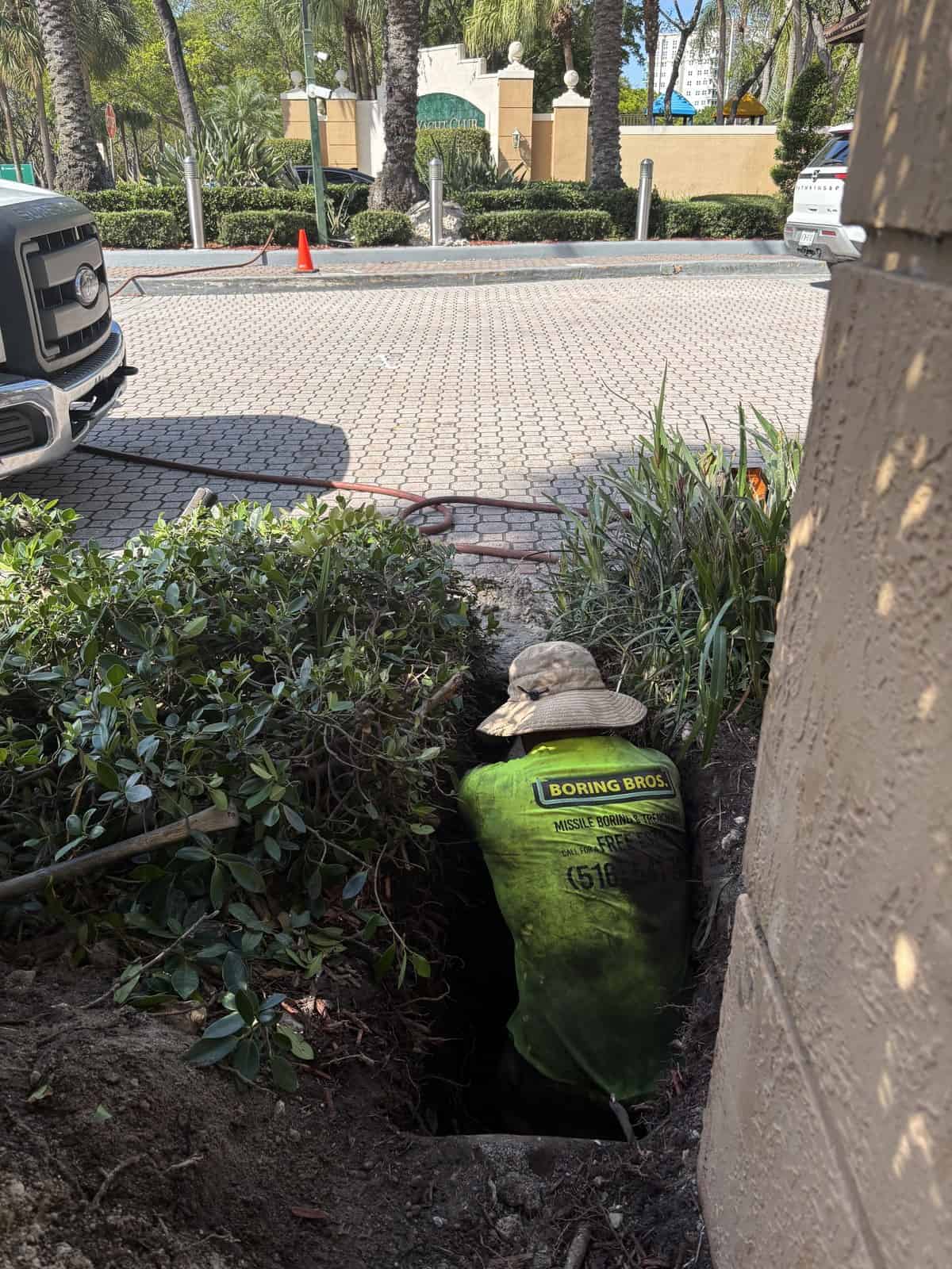 Worker from Boring Bros installing underground utility in a landscaped area.