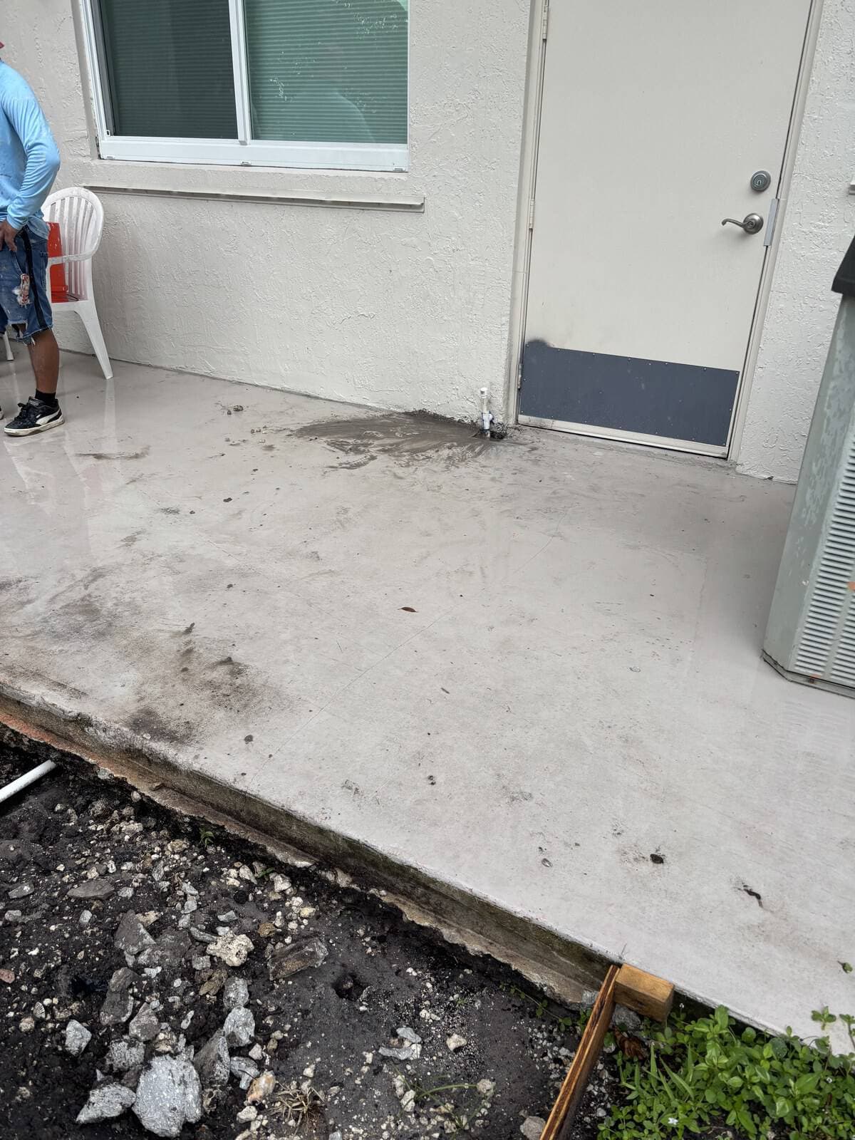 Concrete patio with dirt and debris near a door and window.