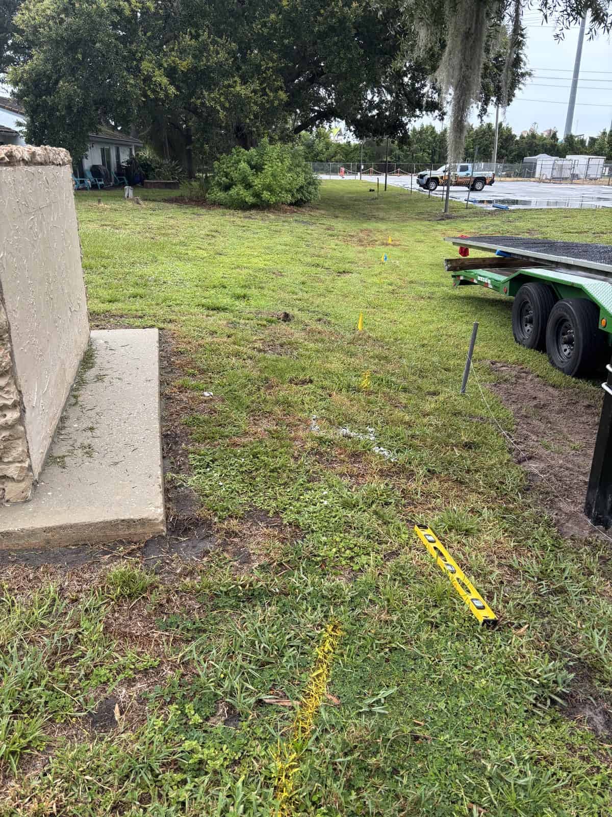 Construction site with green grass, yellow markers, and a trailer on the right.