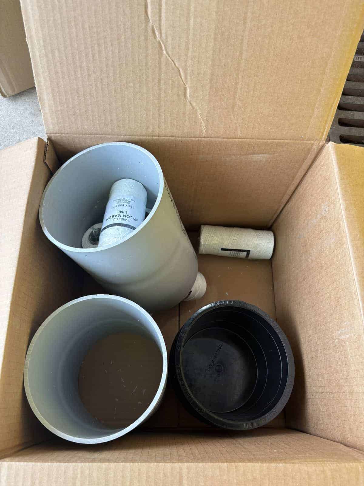 Unopened cardboard box with PVC pipes and fittings inside.
