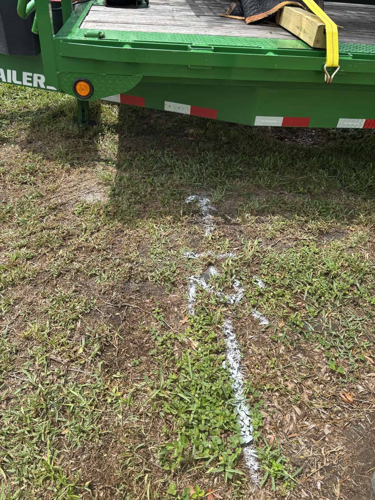 Green utility trailer with safety markings on grass and dirt ground.