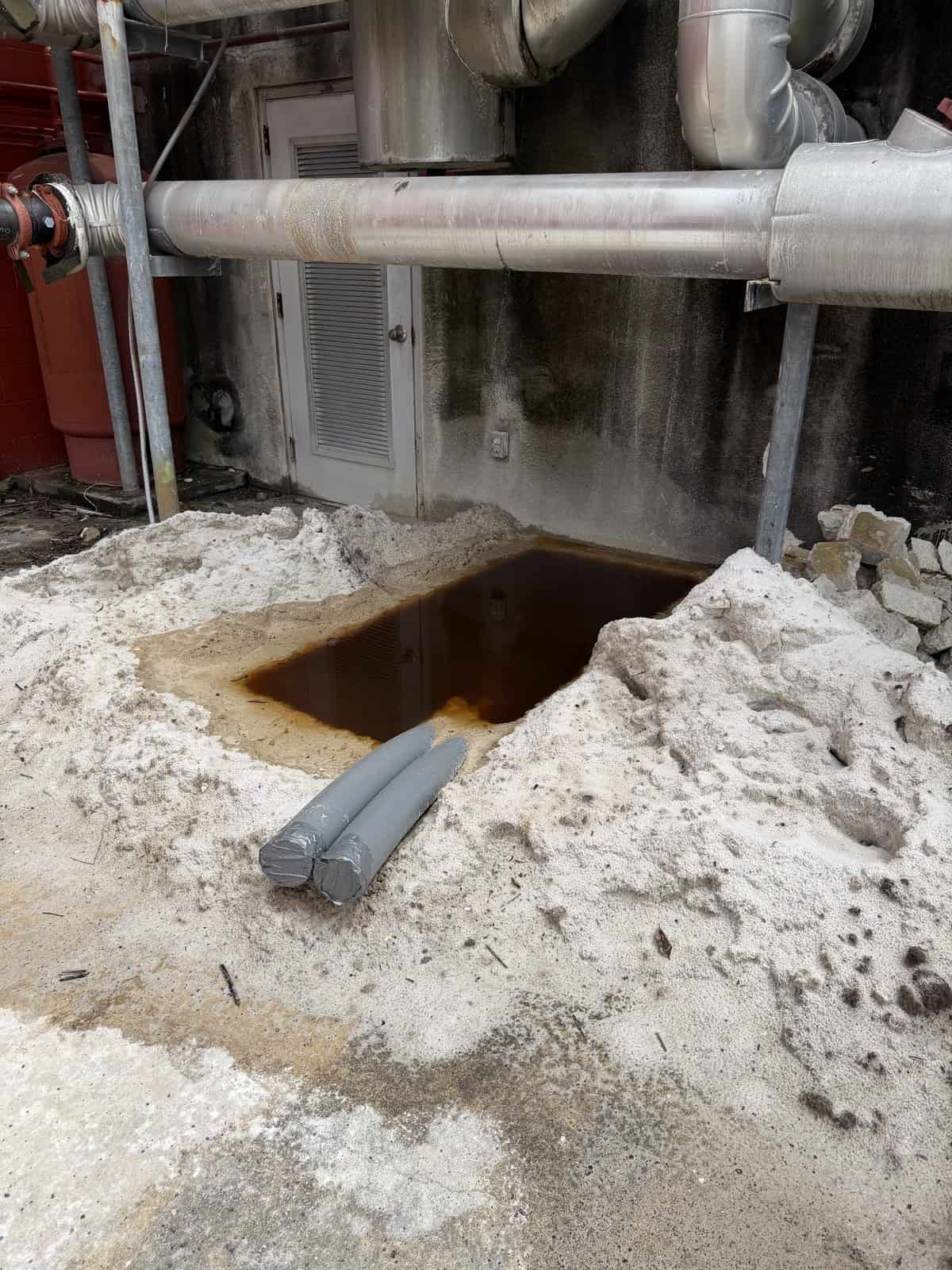 Industrial pipe leak with surrounding sand and water pooling.