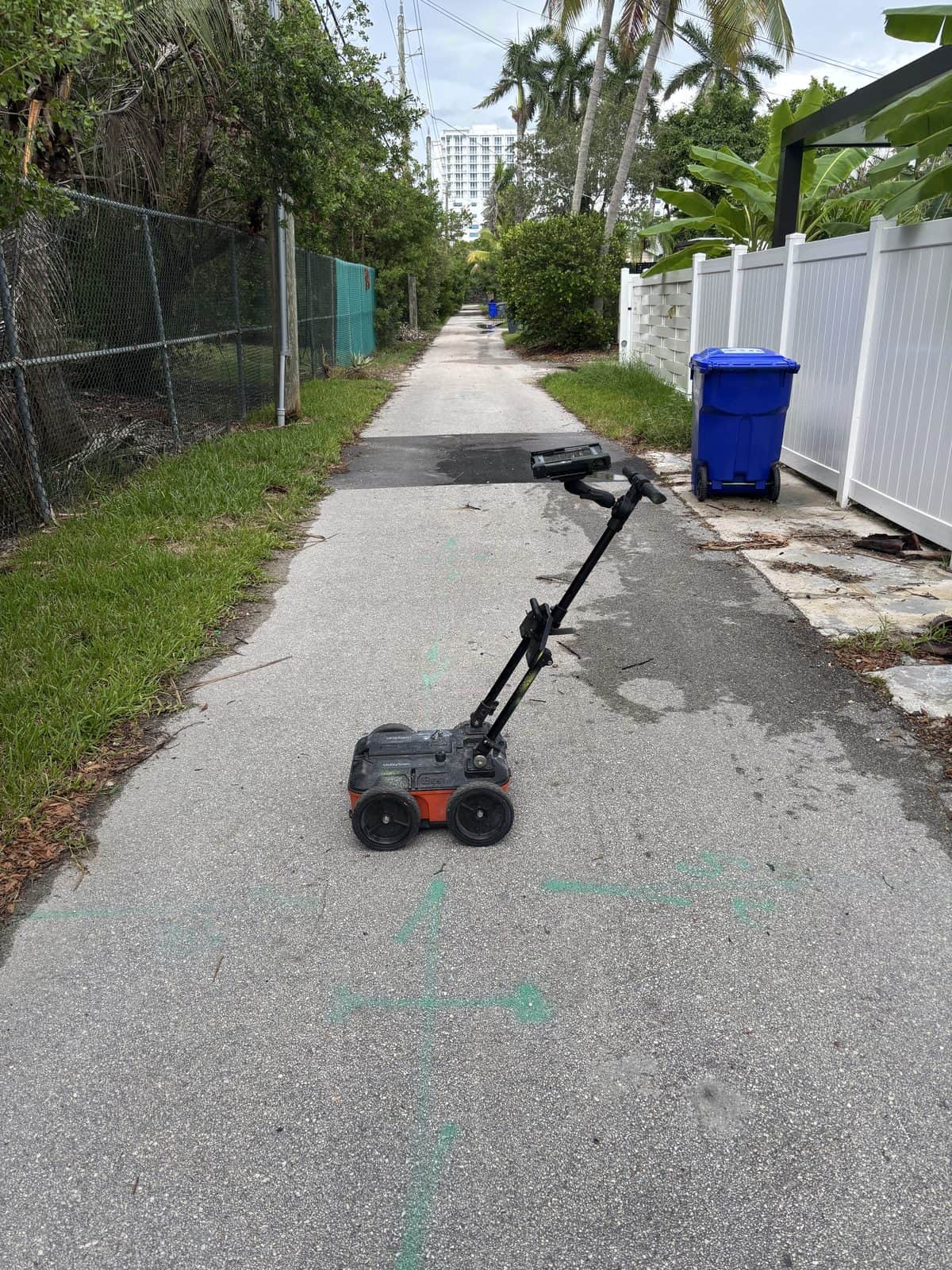 Electric scooter abandoned on sidewalk with greenery and fences nearby.