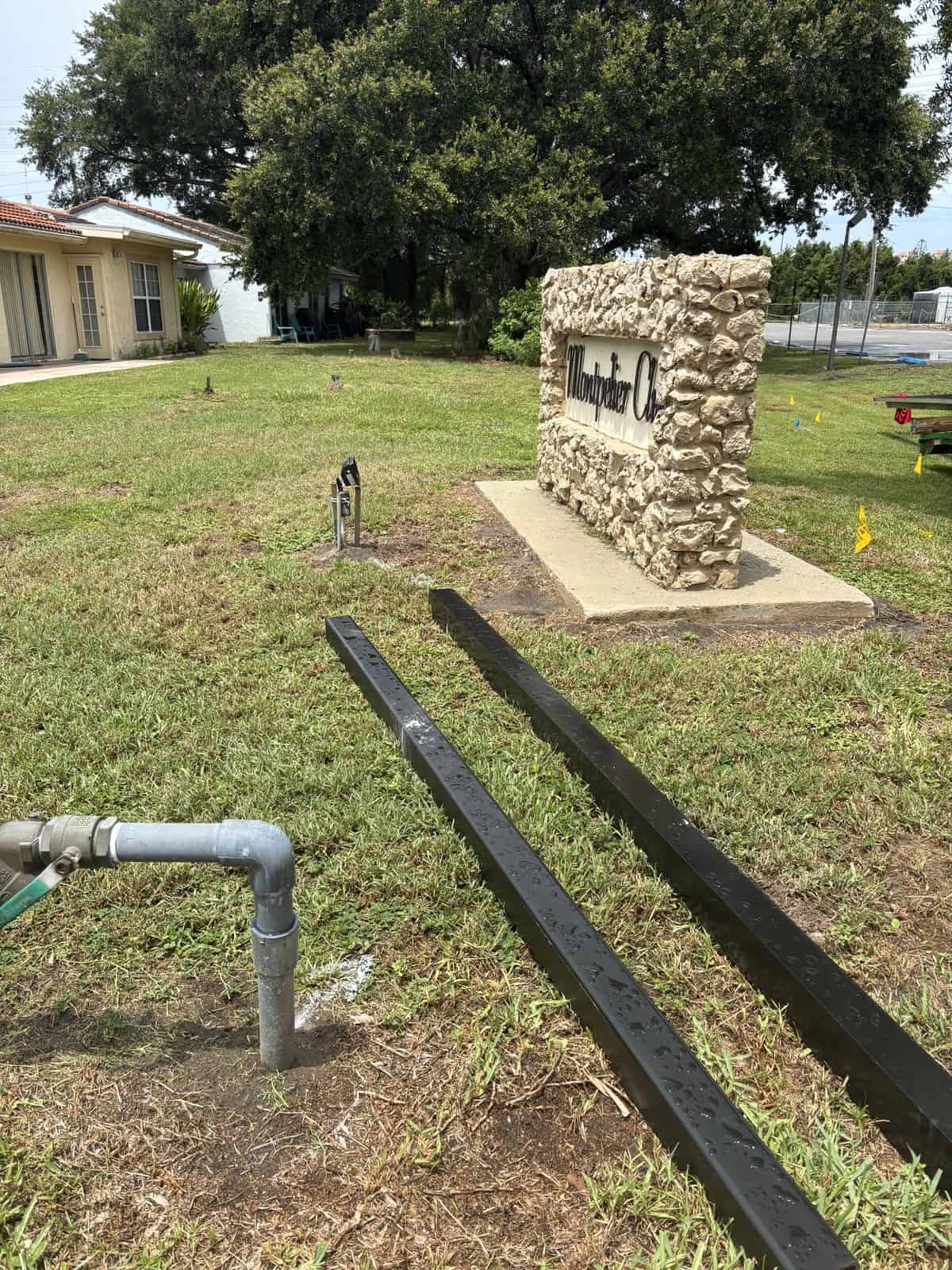 Boring Bros logo on stone monument in a grassy area with trees and buildings nearby.