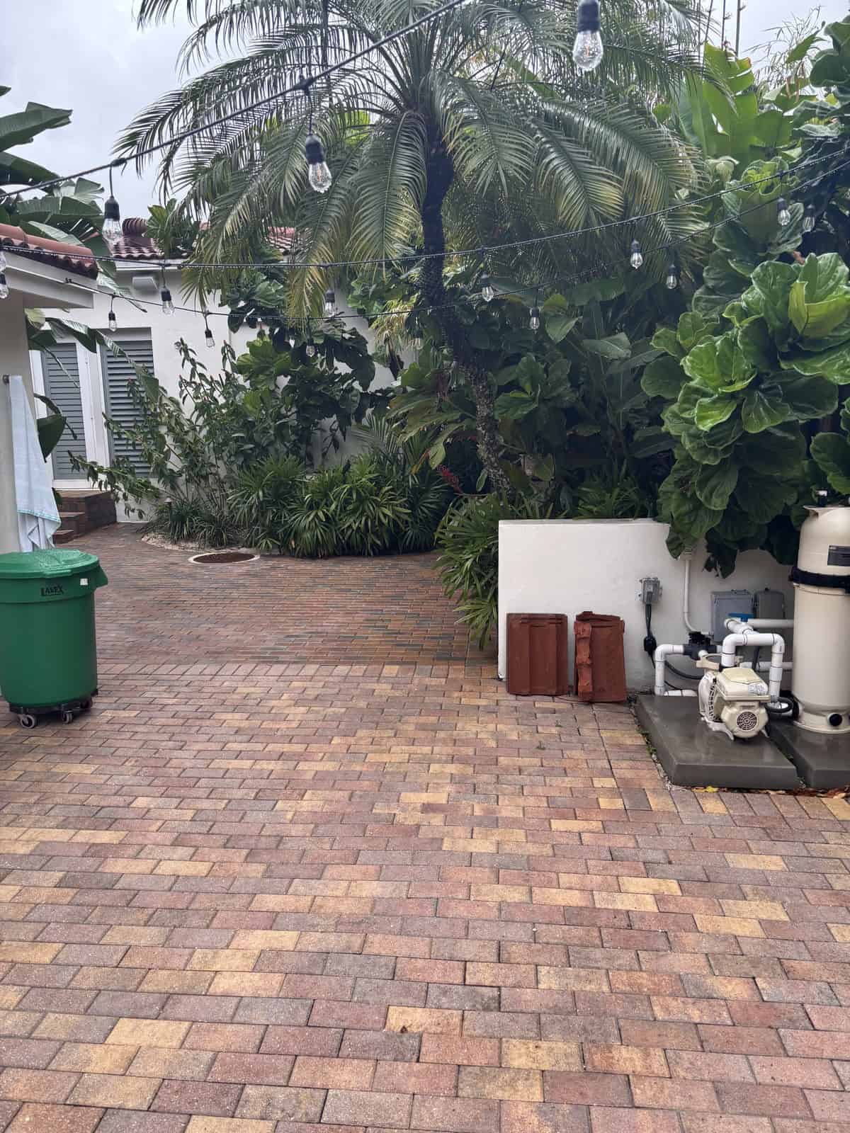 Backyard with brick paving, lush greenery, and outdoor equipment.