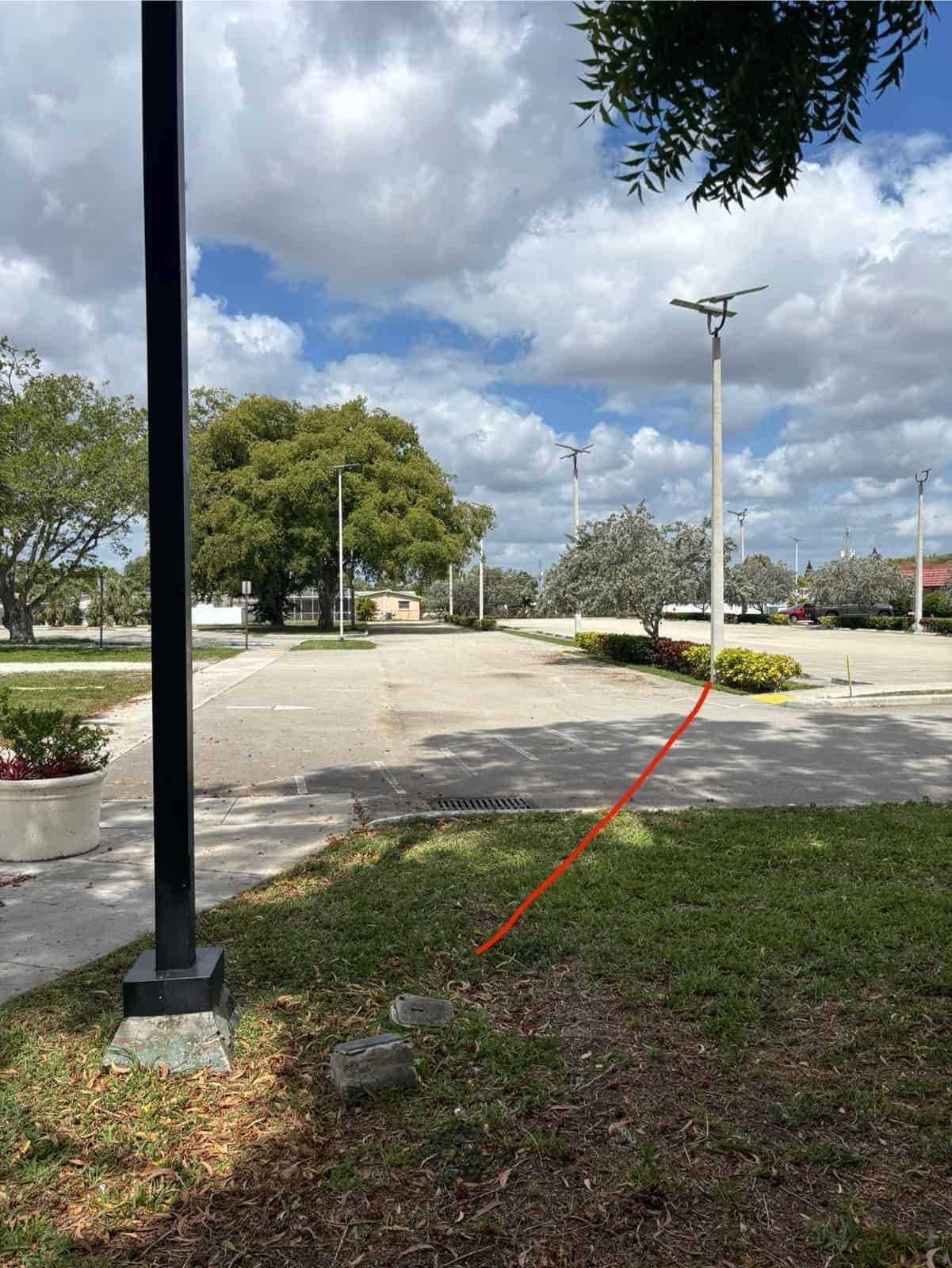 View of an empty parking lot with trees, streetlights, and a partly cloudy sky.