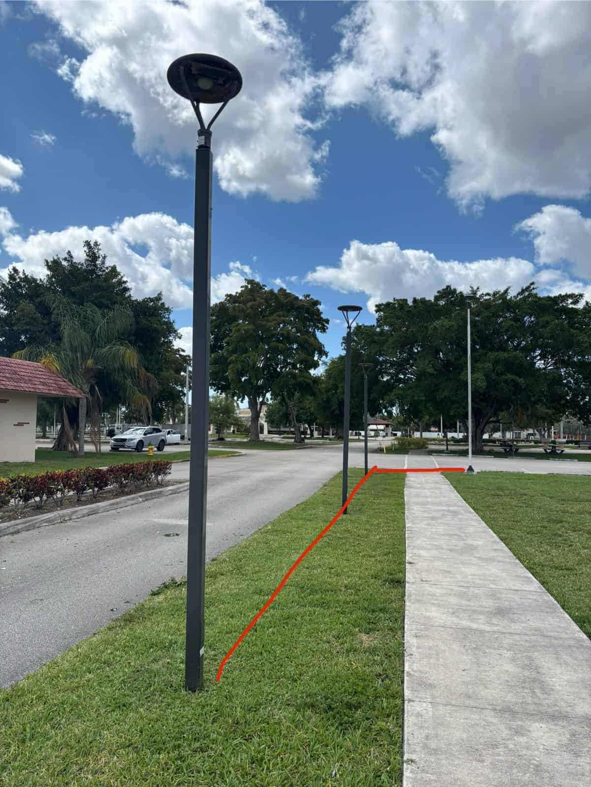Street lamps along a sidewalk in a park setting with trees and cloudy sky.