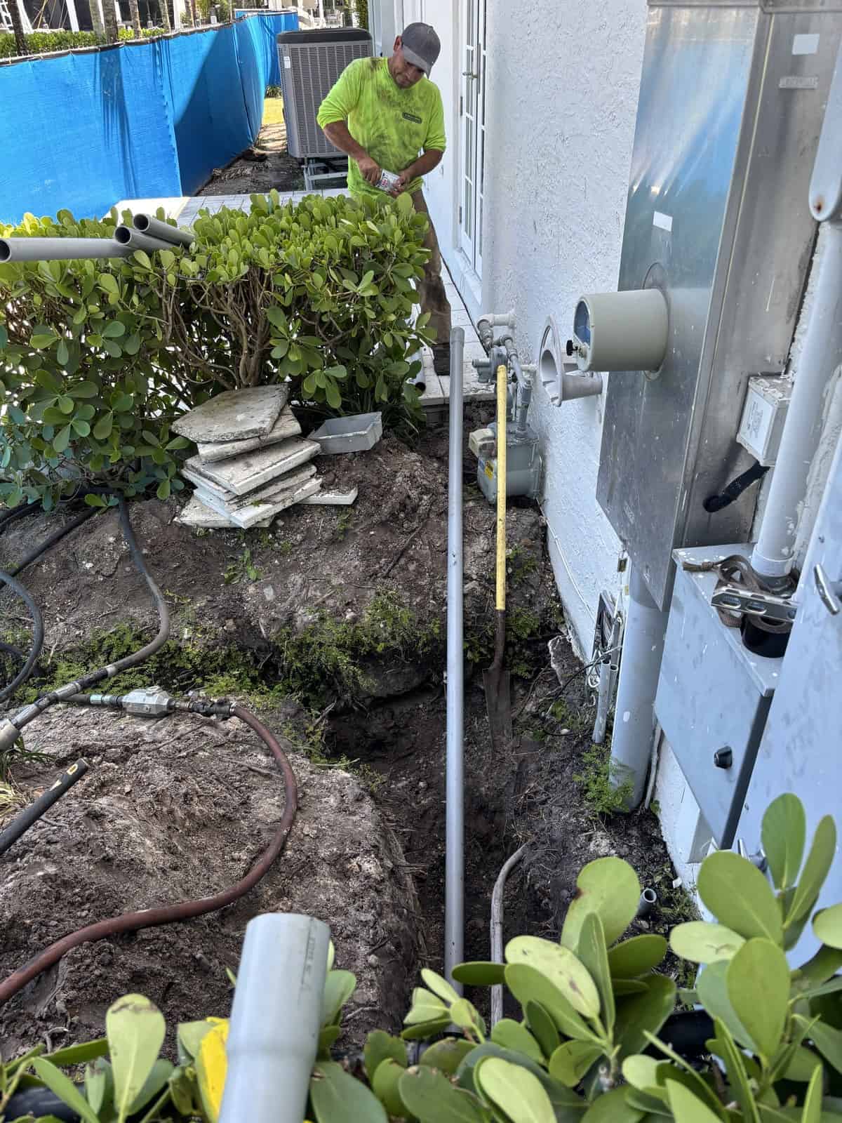 Technician installing underground utility pipe near building exterior.