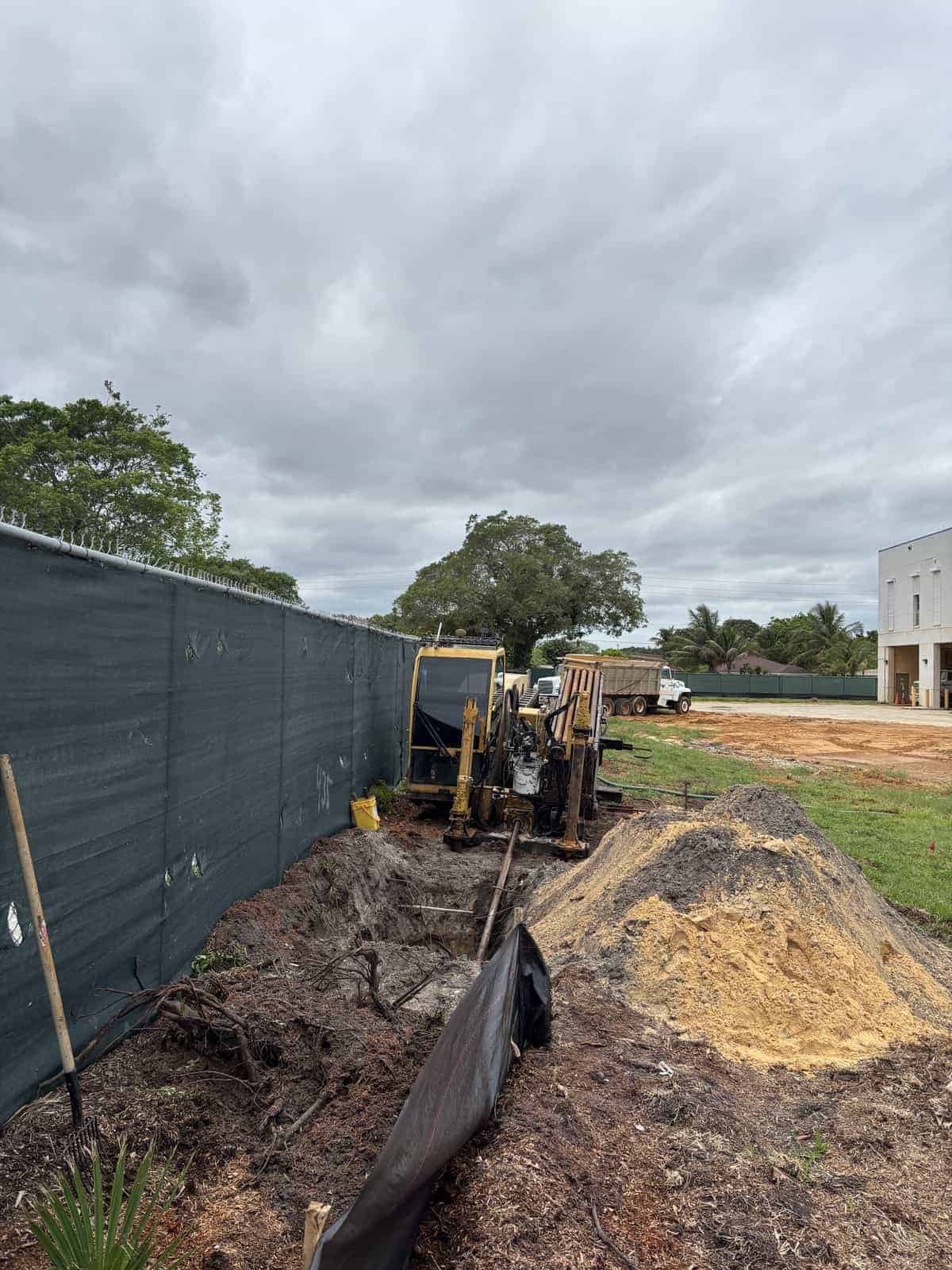 Construction site with excavators and dirt piles under cloudy sky.