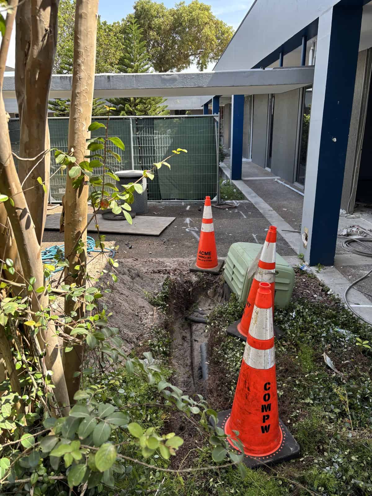 Construction site with orange cones and a trench near a modern building.