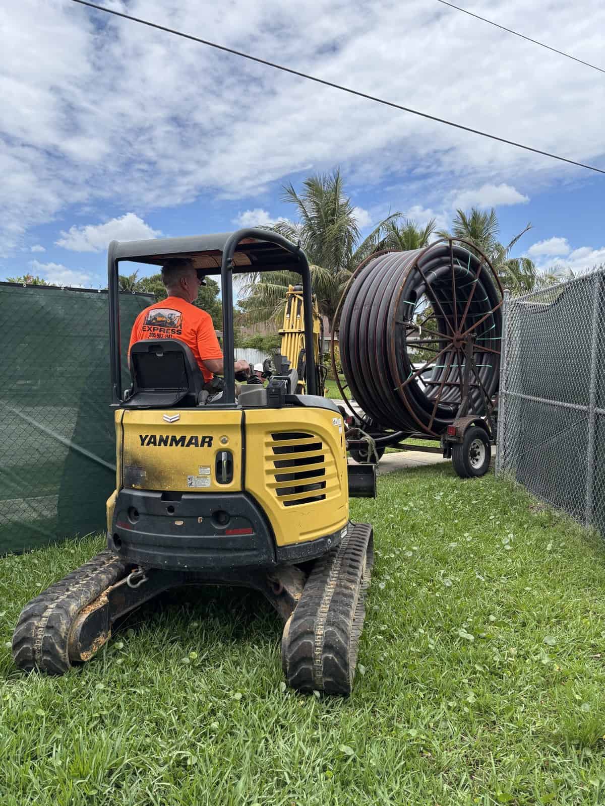 Small yellow Yanmar excavator with a worker operating it outdoors.