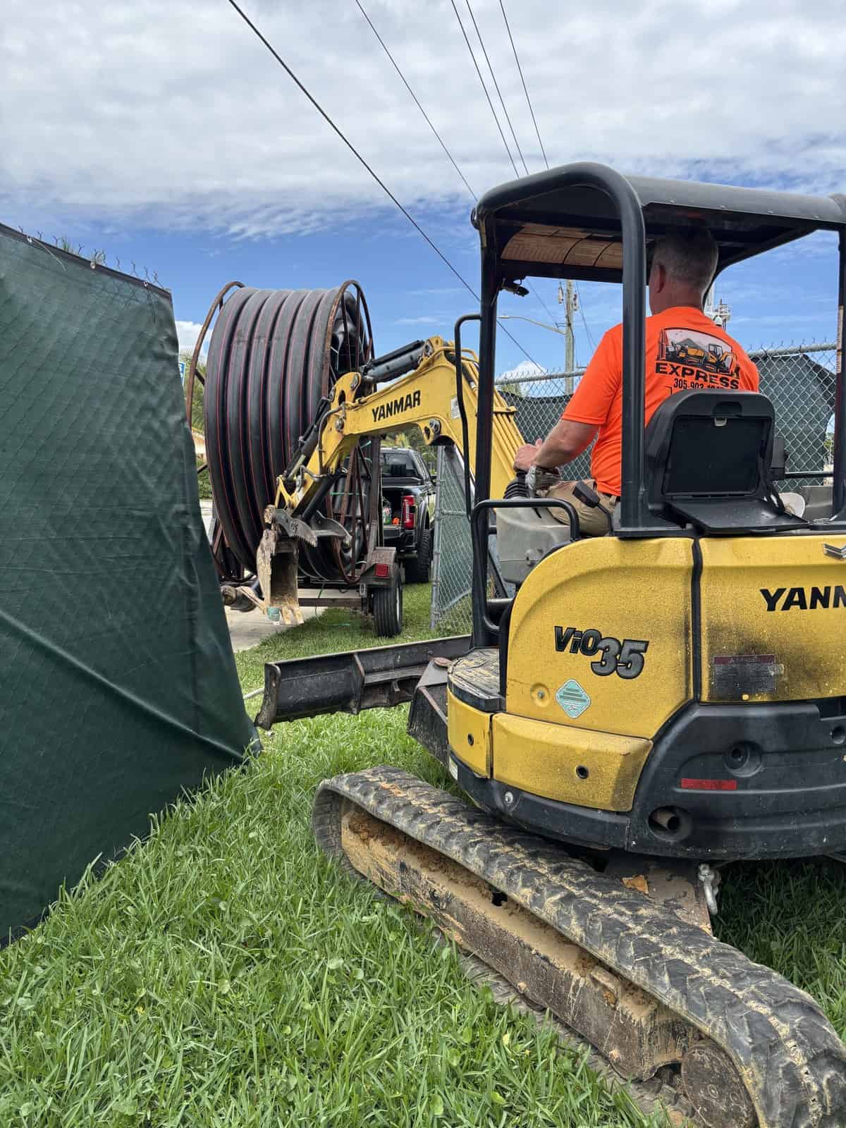 Mini excavator operating near a large cable reel at a construction site.
